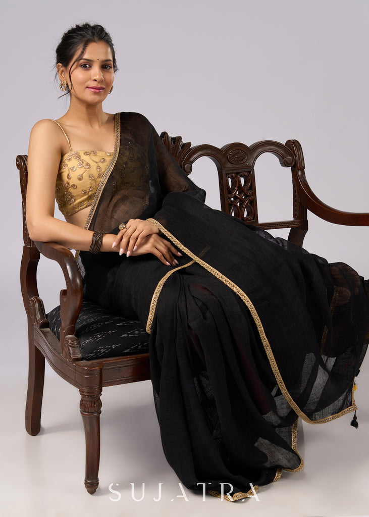 Sophisticated black cotton saree with subtle golden border highlights and pompom